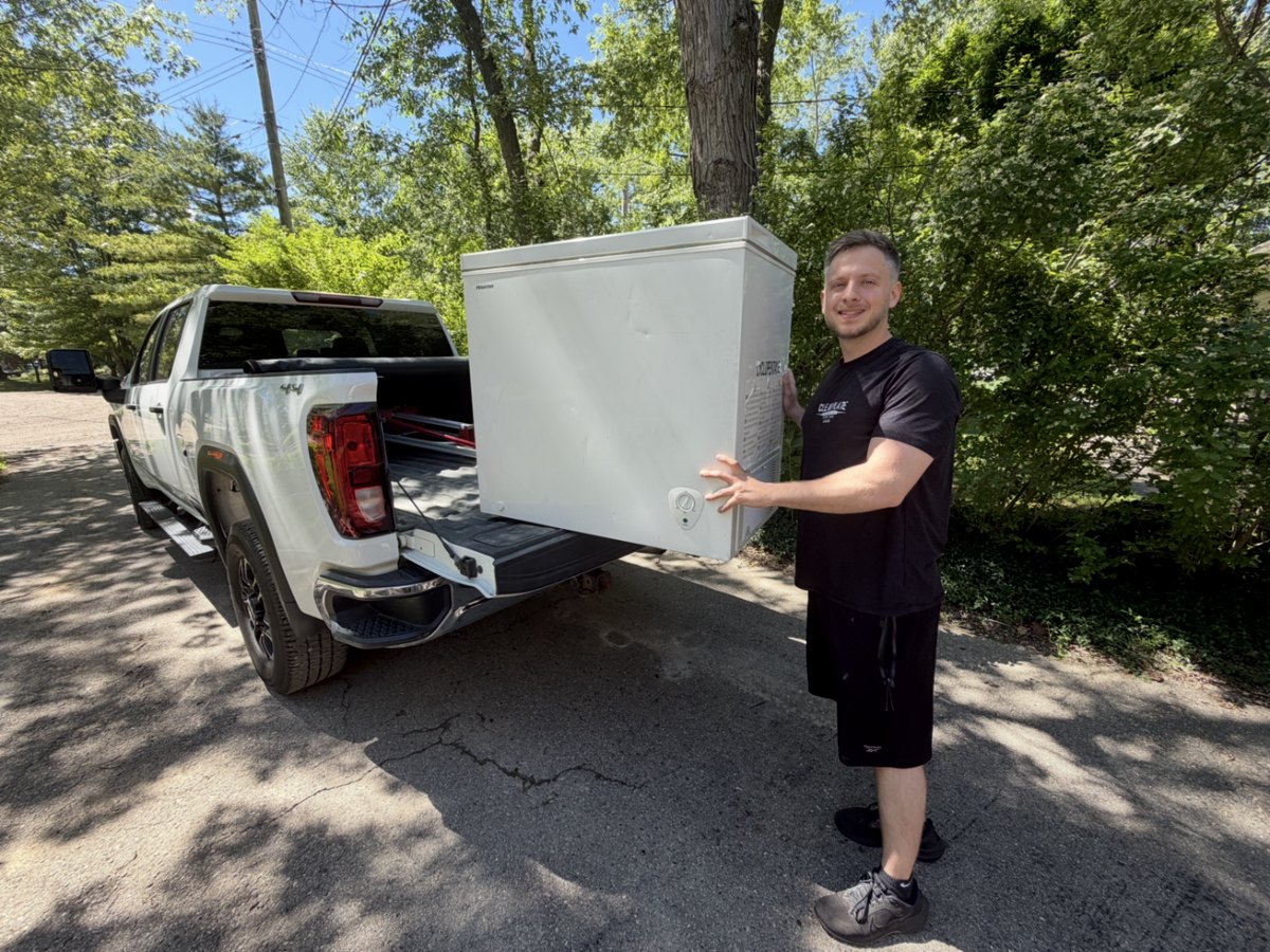 Clean Plate Hauling Co. veteran owner loading a chest freezer into his white GMC Sierra 3500 truck in Metro Detroit